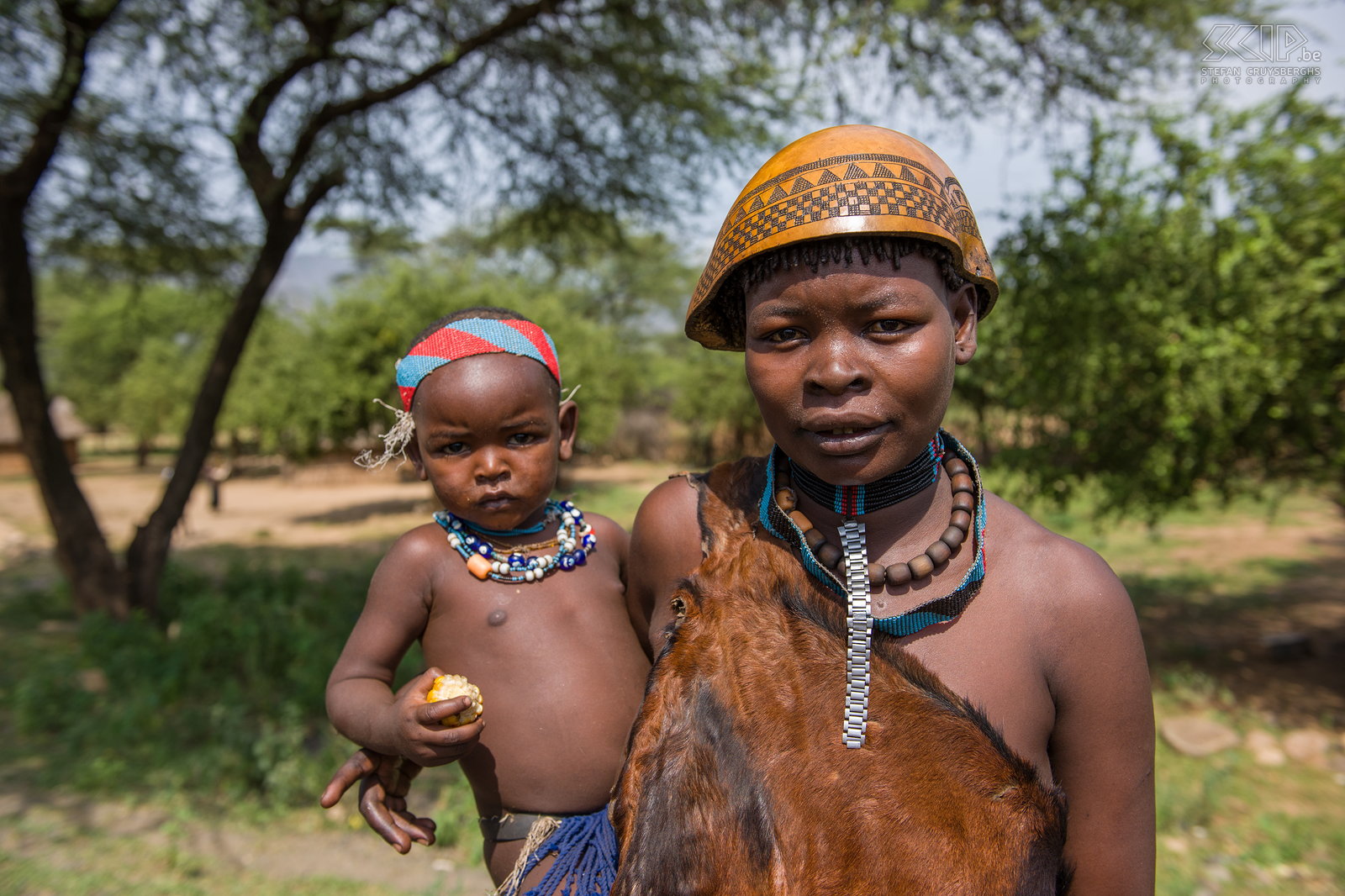 Weyto - Tsemay vrouw met kind We reden verder naar de Omo vallei, het gebied rondom de Omo rivier en het Mago NP in het zuiden van Ethiopië nabij de grenzen van Kenia en Soedan. Deze regio is het woongebied van een 20-tal etnische groepen zoals de Tsemai, Ari, Mursi, Hamer, Surma, Dassanech, Karo, Nyangatom, Banna, Arebore, ... die allen nog eigen tradities, ceremonies en unieke lichaams-versieringen kennen. Littekenpatronen, lichaamsbeschilderingen, arm- en enkelbanden, ingenieuze vlechtkapsels, kralen en lipschotels, ... het zijn allen eeuwenoude kunstzinnige uitingen. <br />
<br />
De eerste stam waarvan we een dorpje bezoeken zijn de Tsemai/Tsemay/Tsamai in de buurt van het stadje Weyto. Het zijn landbouwers en veehouders die ook bijenkorven ophangen voor honingproductie. Veel Tsemai vrouwen dragen kleding gemaakt van leder en soms ook een kalebas als hoofddeksel. Stefan Cruysberghs